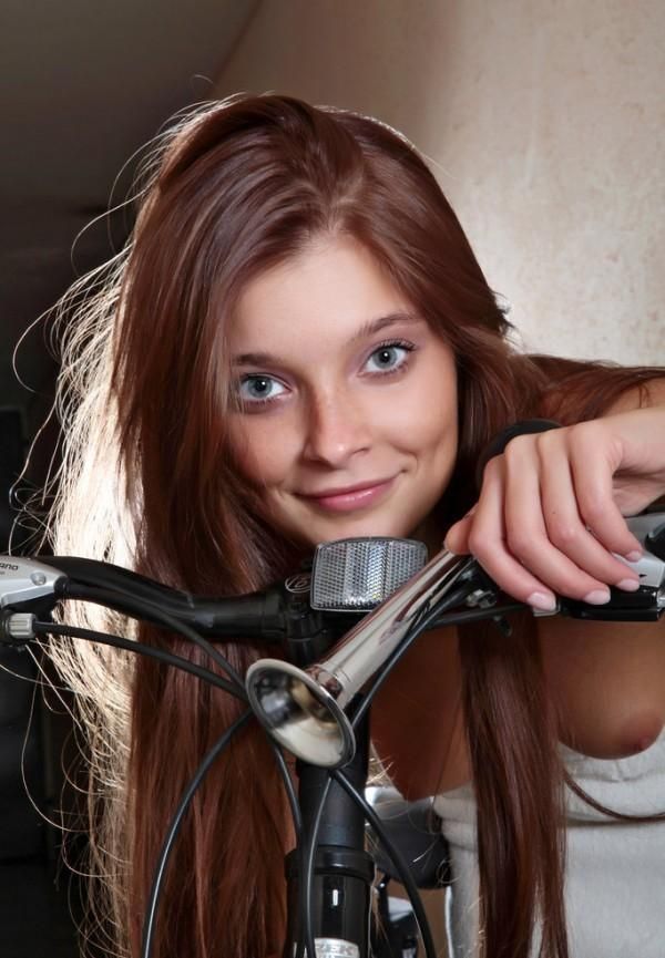 cute young brunette girl with long hair and blue eyes posing near the bicycle