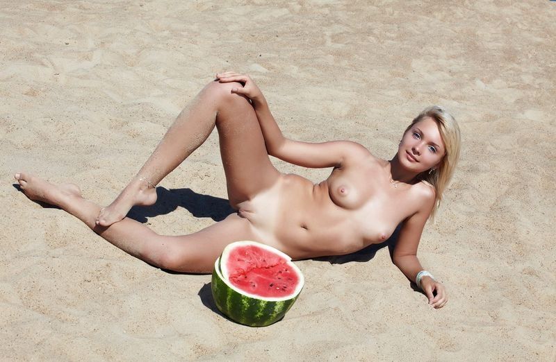 young blonde girl on the beach eating a watermelon