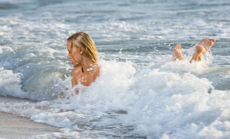 young blonde girl on the beach shows off her body in sea waves
