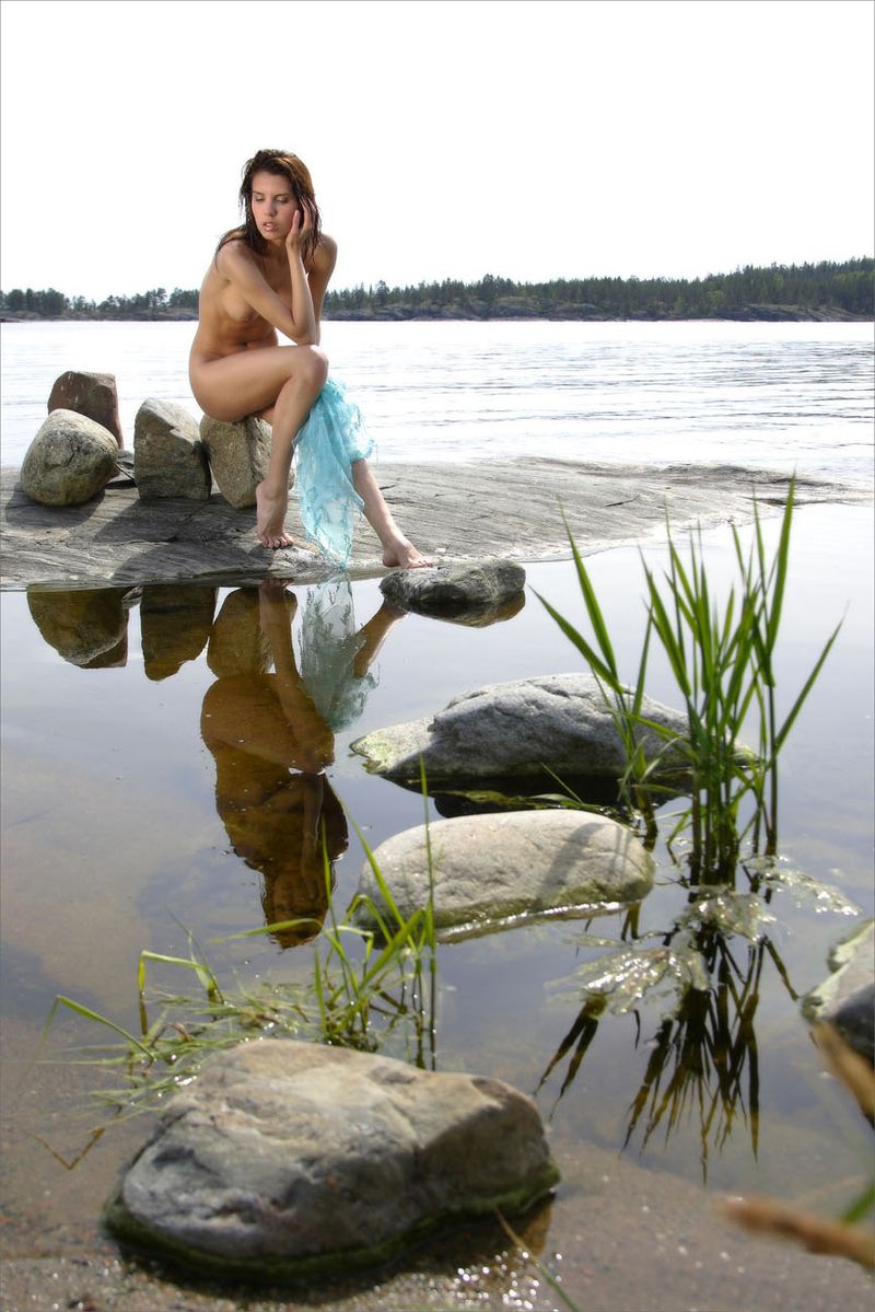 young brunette girl at the lake on rocks with a blue scarf