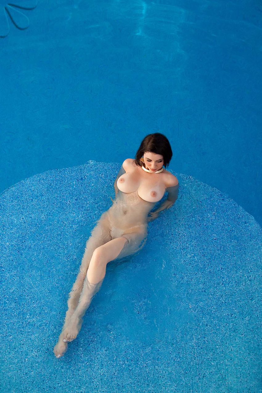 brunette girl with a golden gorget necklace, navel piercing and earrings shows off in the swimming pool