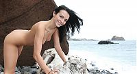 Babes: young black haired girl reveals her short jeans on the driftwood on the rocky shore at the sea