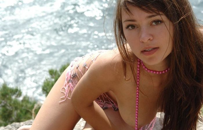 young brunette girl wearing a pink necklace on rocks above the sea