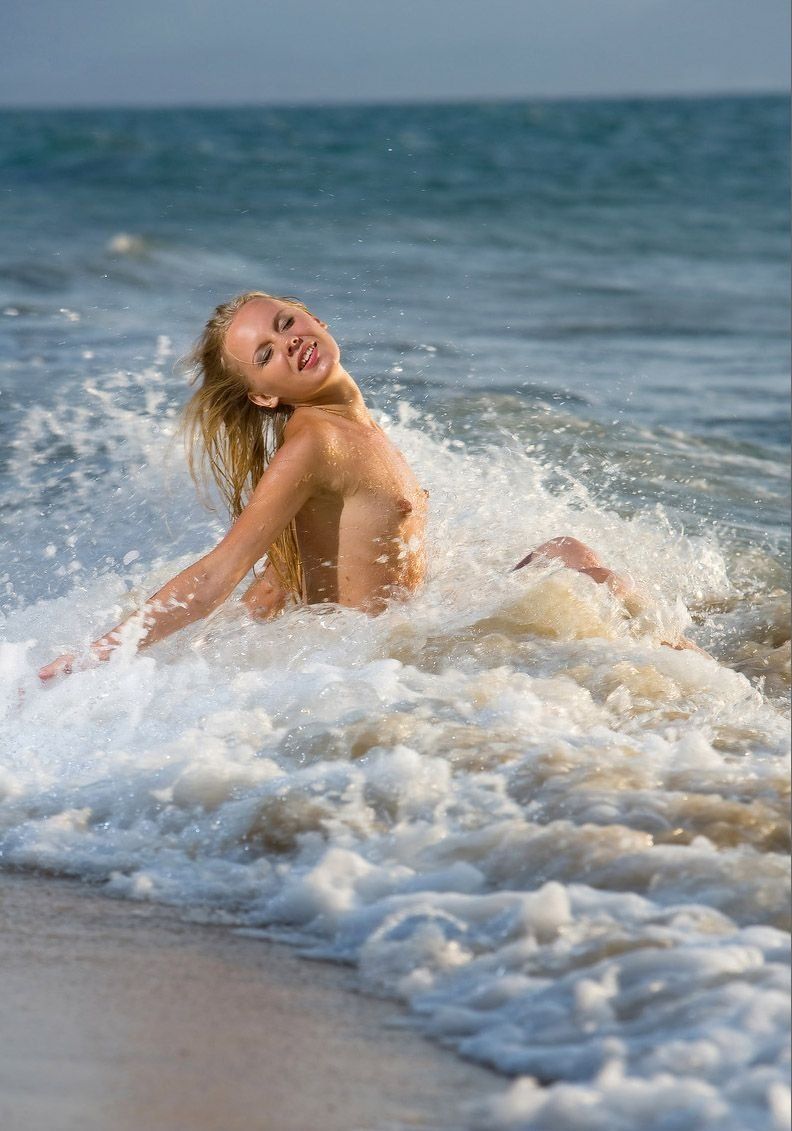 young blonde girl on the beach shows off her body in sea waves