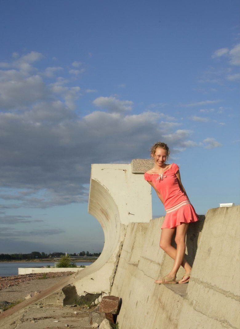 young curly blonde girl in pink dress near concrete walls