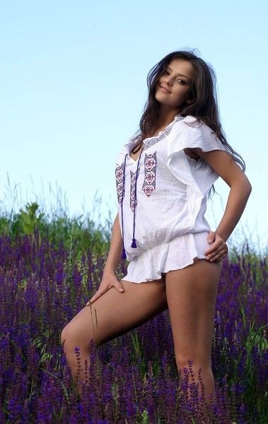 cute young brunette girl reveals on the field of wild flowers