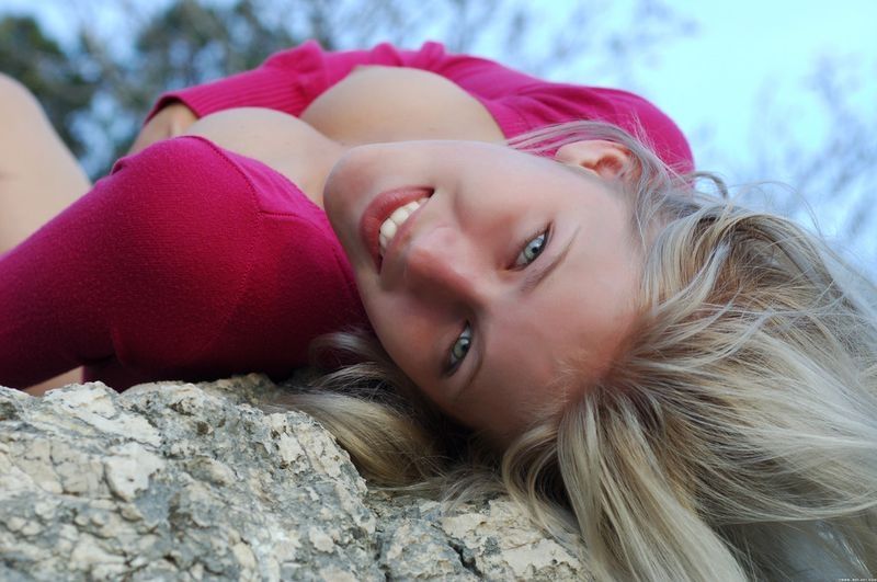 cute young blonde girl posing on rocks in a tight pink sweater