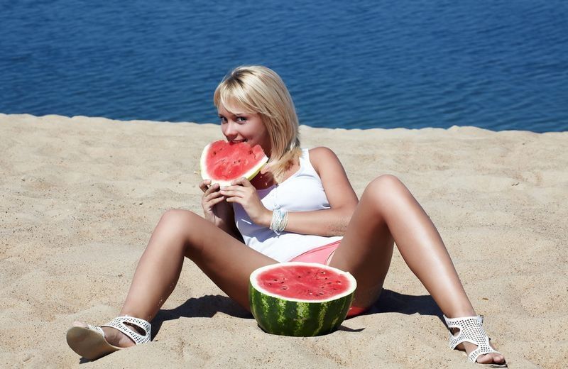 young blonde girl on the beach eating a watermelon