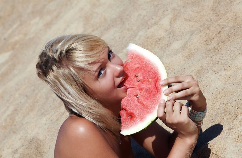 young blonde girl on the beach eating a watermelon