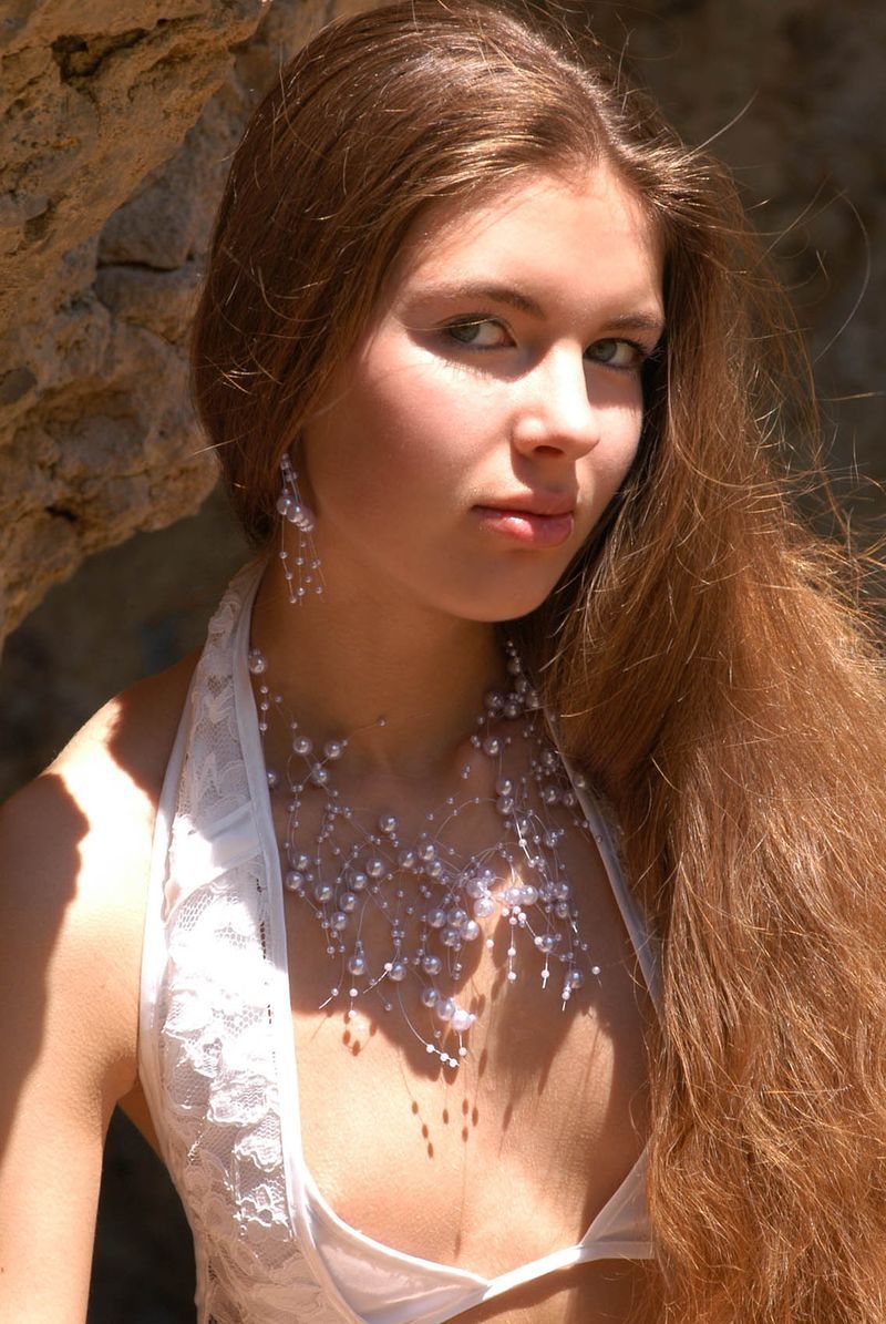 cute young brunette girl wearing a white lingerie on rocks at the sea