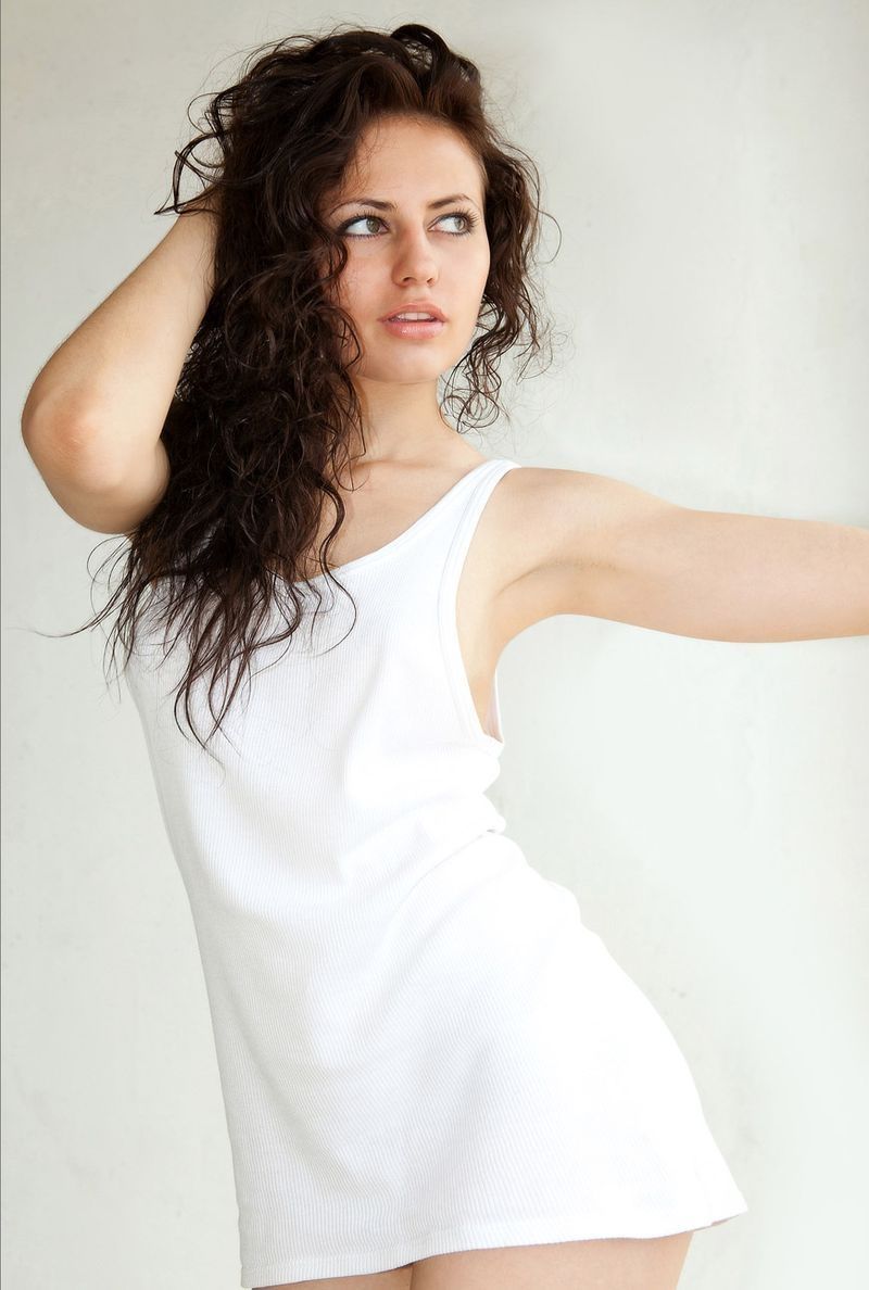 curly brunette girl reveals a white chemise on the carpet with a wooden folding chair