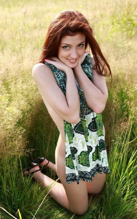 red haired girl undresses a green dress on the field