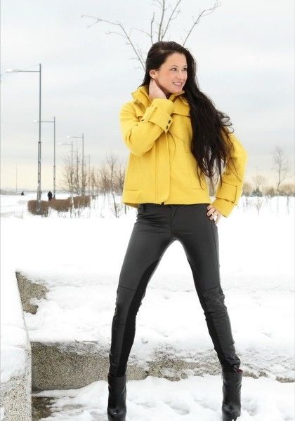 young brunette girl undresses a yellow coat and black leather pants outdoors in the winter