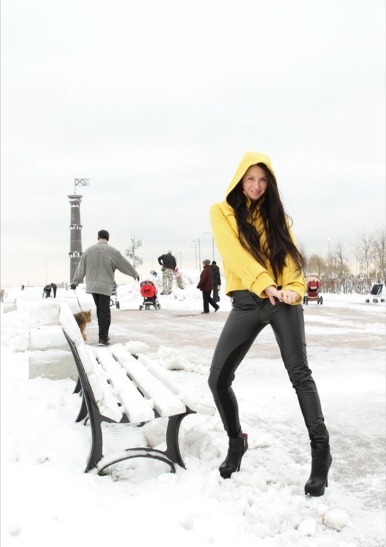 young brunette girl undresses a yellow coat and black leather pants outdoors in the winter