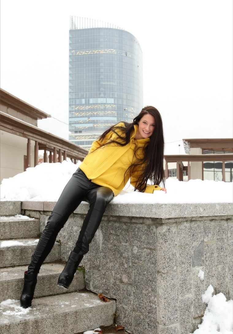 young brunette girl undresses a yellow coat and black leather pants outdoors in the winter