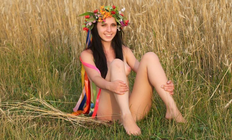 young brunette girl with a flower wreath on the wheat field