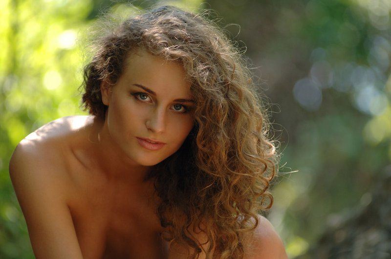 young curly brunette girl naked on rocks in the forest