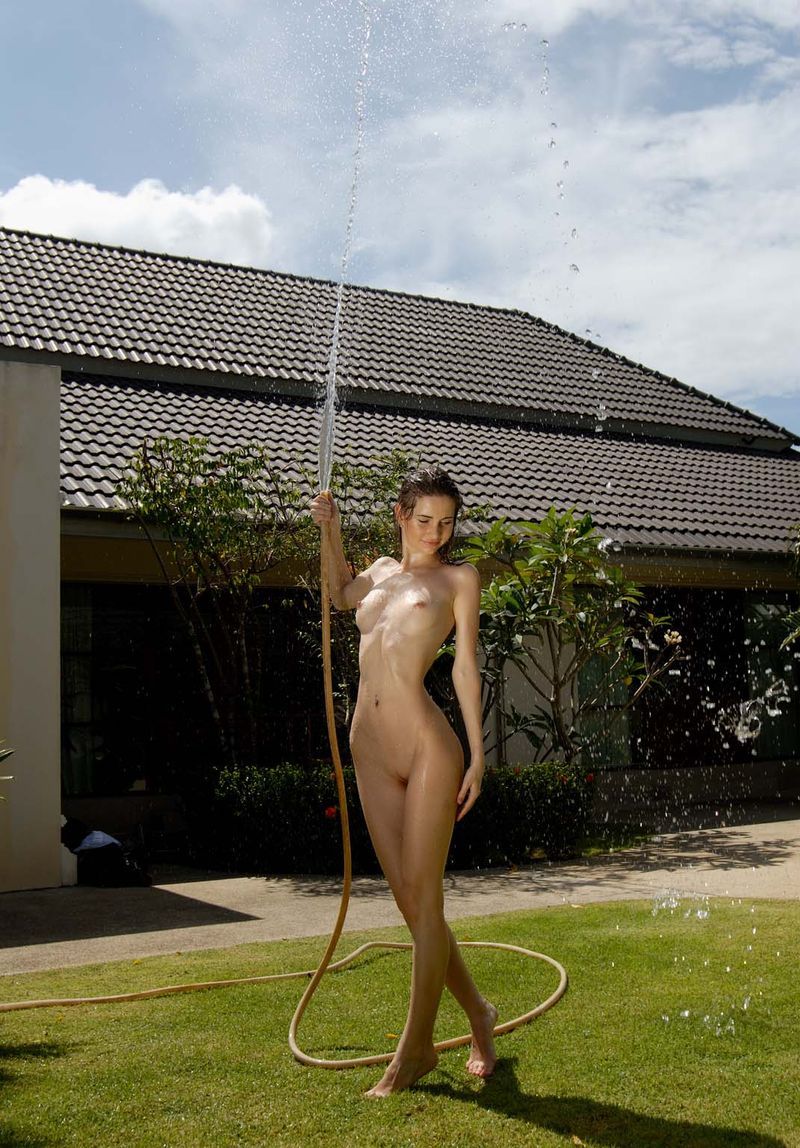 young brunette girl getting wet on the backyard lawn