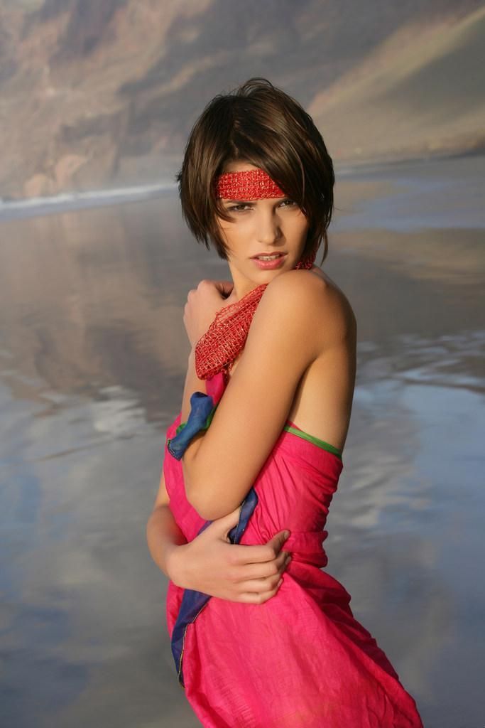 young brunette girl wearing a headband and posing on the beach with a colorful scarf