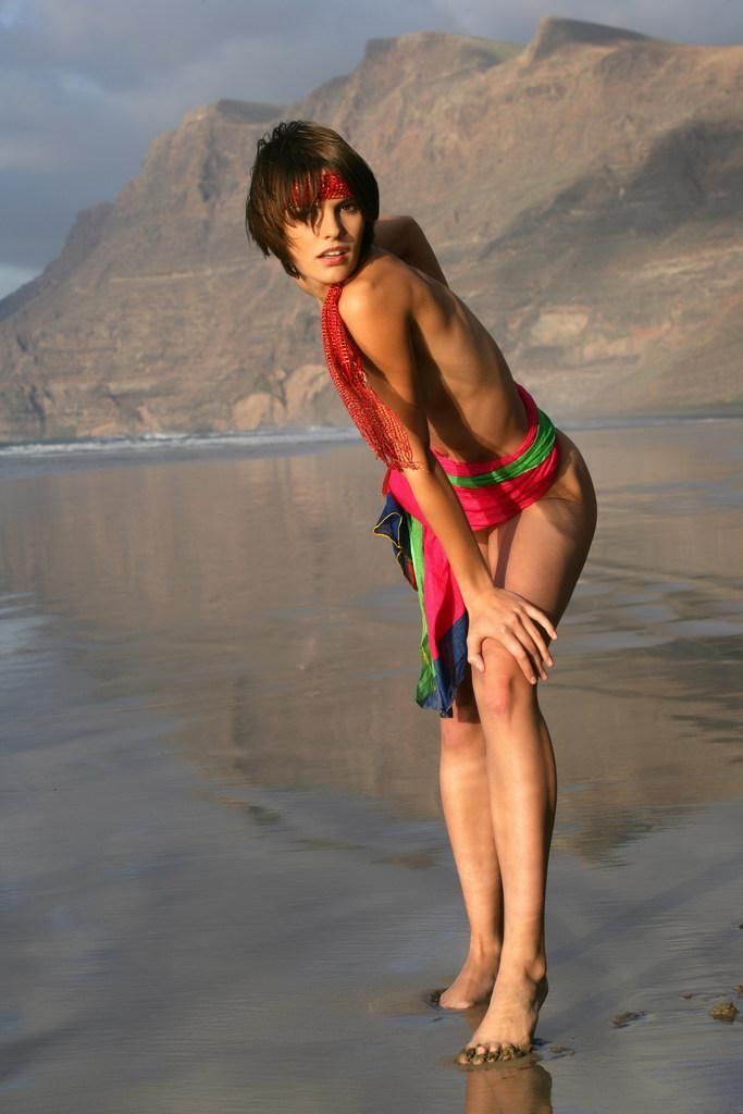 young brunette girl wearing a headband and posing on the beach with a colorful scarf