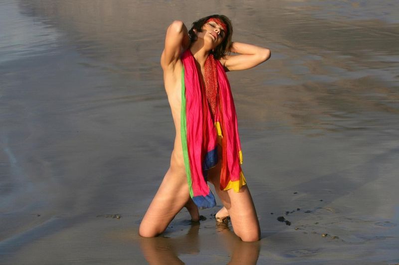 young brunette girl wearing a headband and posing on the beach with a colorful scarf