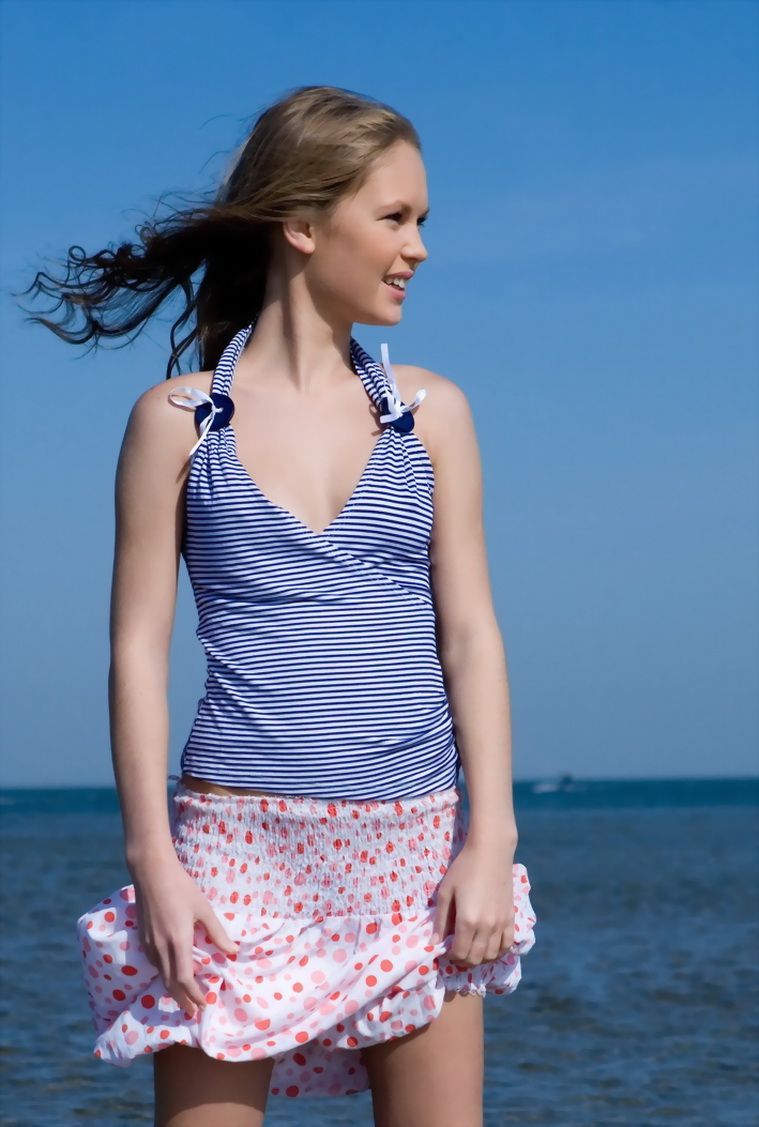 cute young blonde girl undresses at the sea shoreline