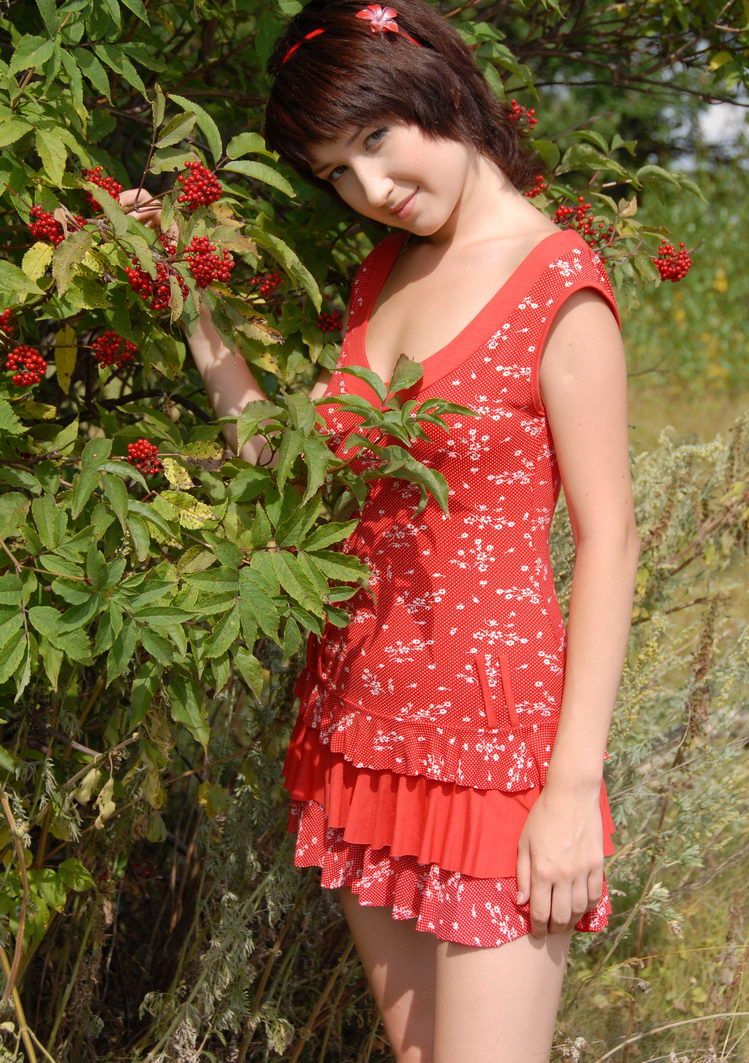 young brunette girl strips her dress near mountain-ash shrubs with red berries