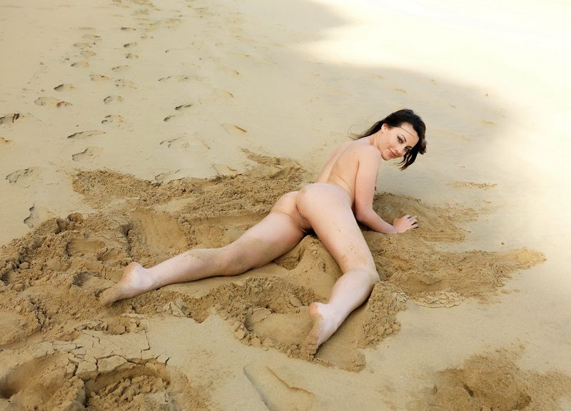 young black haired girl in the sand on the rocky shore with the rough sea