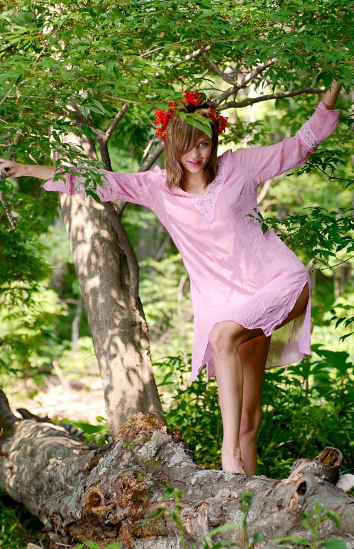 young dark blonde girl with blue eyes and a floral wreath reveals a pink nightgown in the forest
