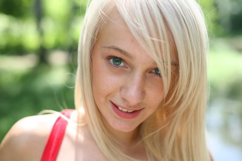 cute young blonde girl with blue eyes reveals on the bridge in a red white dress
