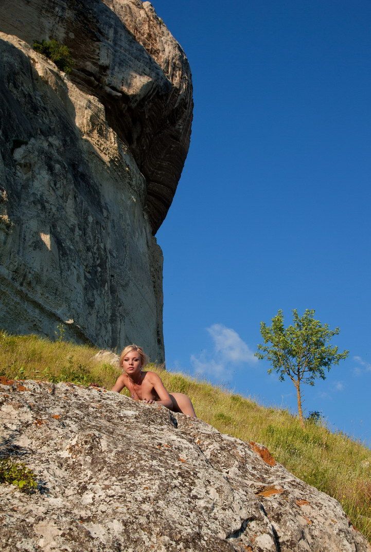 blonde girl reveals with a pink necklace and negligee outside on the hill with rocks