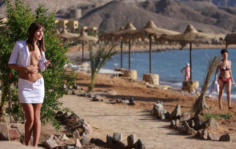 young brunette girl reveals her white top and skirt at the hotel on the beach