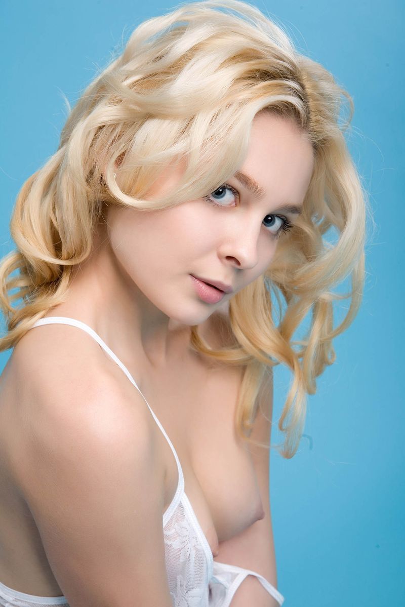 young curly blonde girl wearing a white chemise in the blue studio