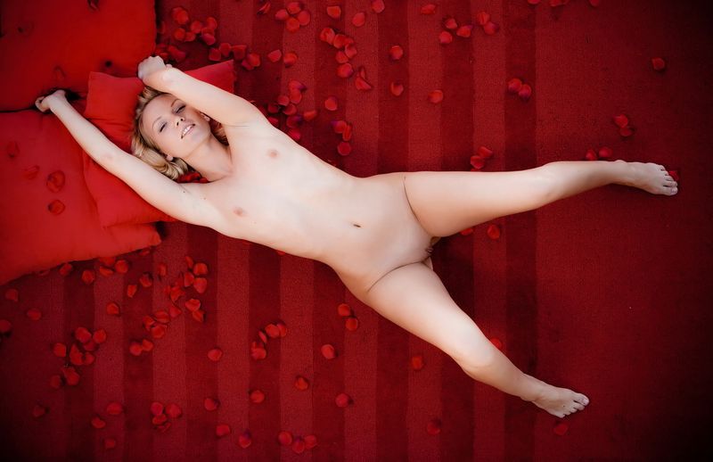 young blonde girl shows off on the red bed with petals leaves