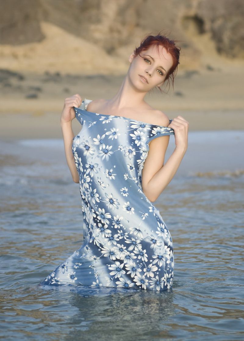 young red haired girl undresses her dress with flowers in the sea