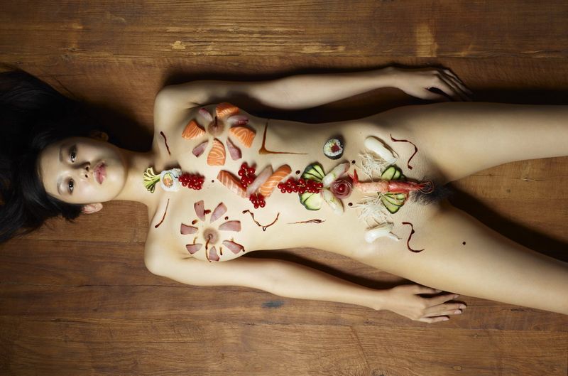 two asian japanese girls practicing a nyotaimori and serving sushi on a naked woman's body