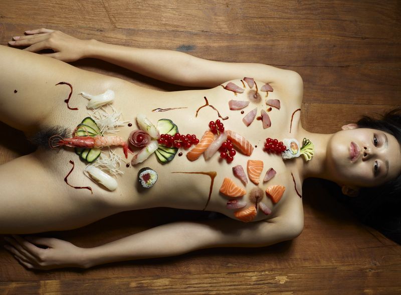 two asian japanese girls practicing a nyotaimori and serving sushi on a naked woman's body