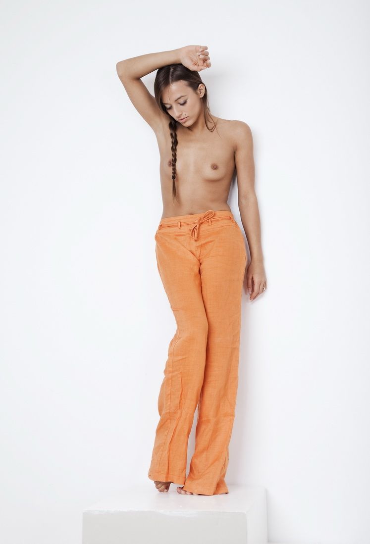 young brunette girl with large labia minora undresses her orange trousers in the studio