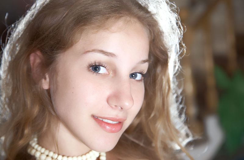 young curly blonde girl wearing a white necklace on the rattan armchair with a red velvet fabric