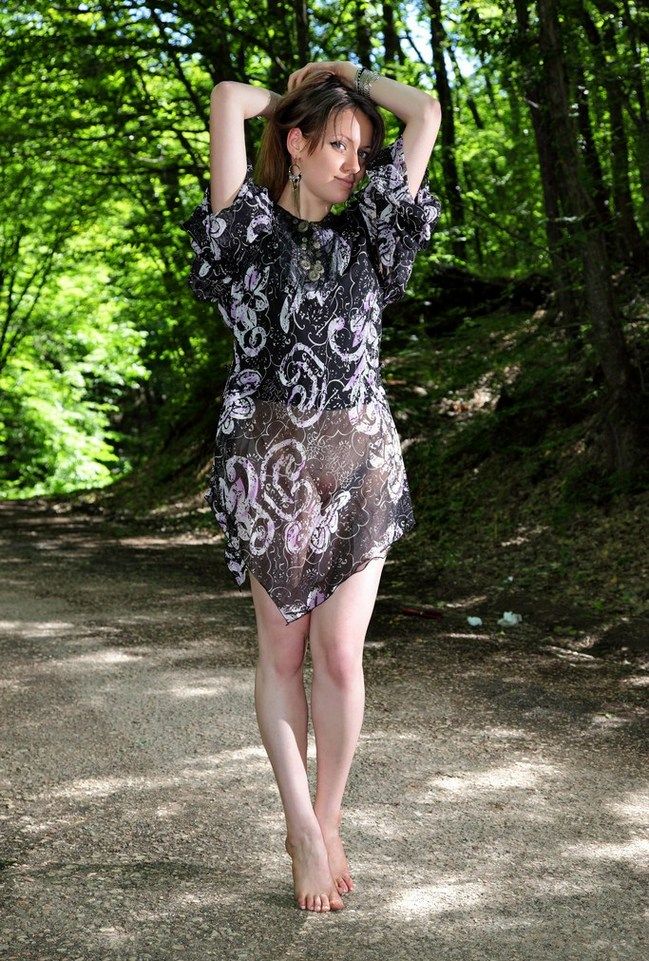 young brunette girl with long hair and blue eyes strips her dress on the forest pathway