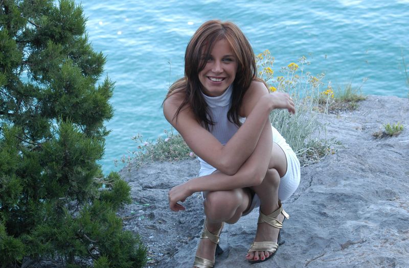 young red haired girl with blue eyes undresses her white dress on rocky hill at the sea