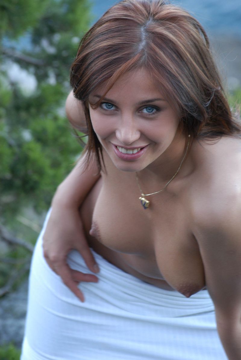 young red haired girl with blue eyes undresses her white dress on rocky hill at the sea