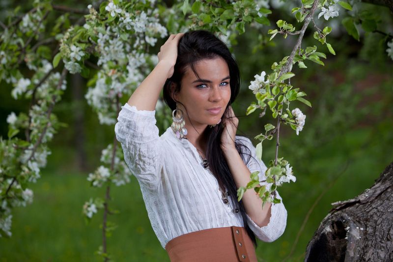 young black haired girl with blue eyes reveals on the green glade with a spring tree