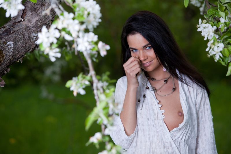 young black haired girl with blue eyes reveals on the green glade with a spring tree