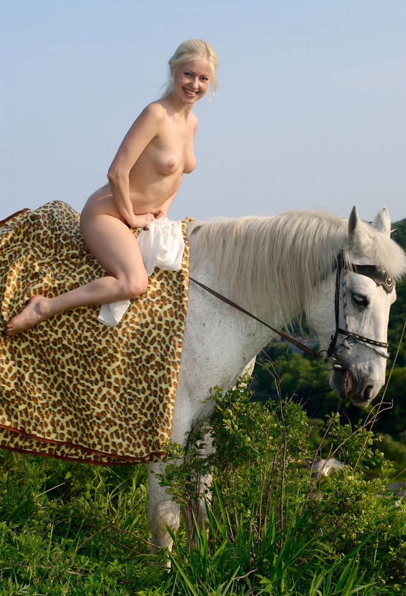 young blonde girl with a white top riding on the white horse in the nature