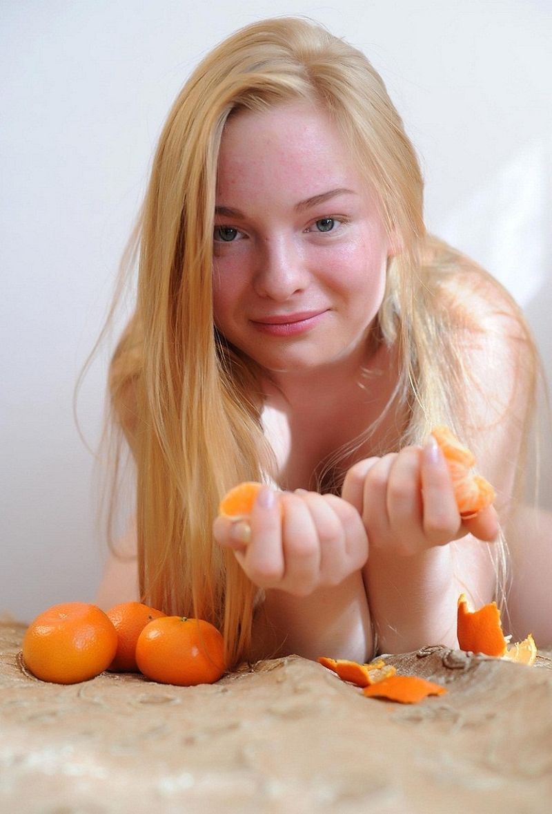 young reddish blonde girl posing on the old couch while eating mandarins