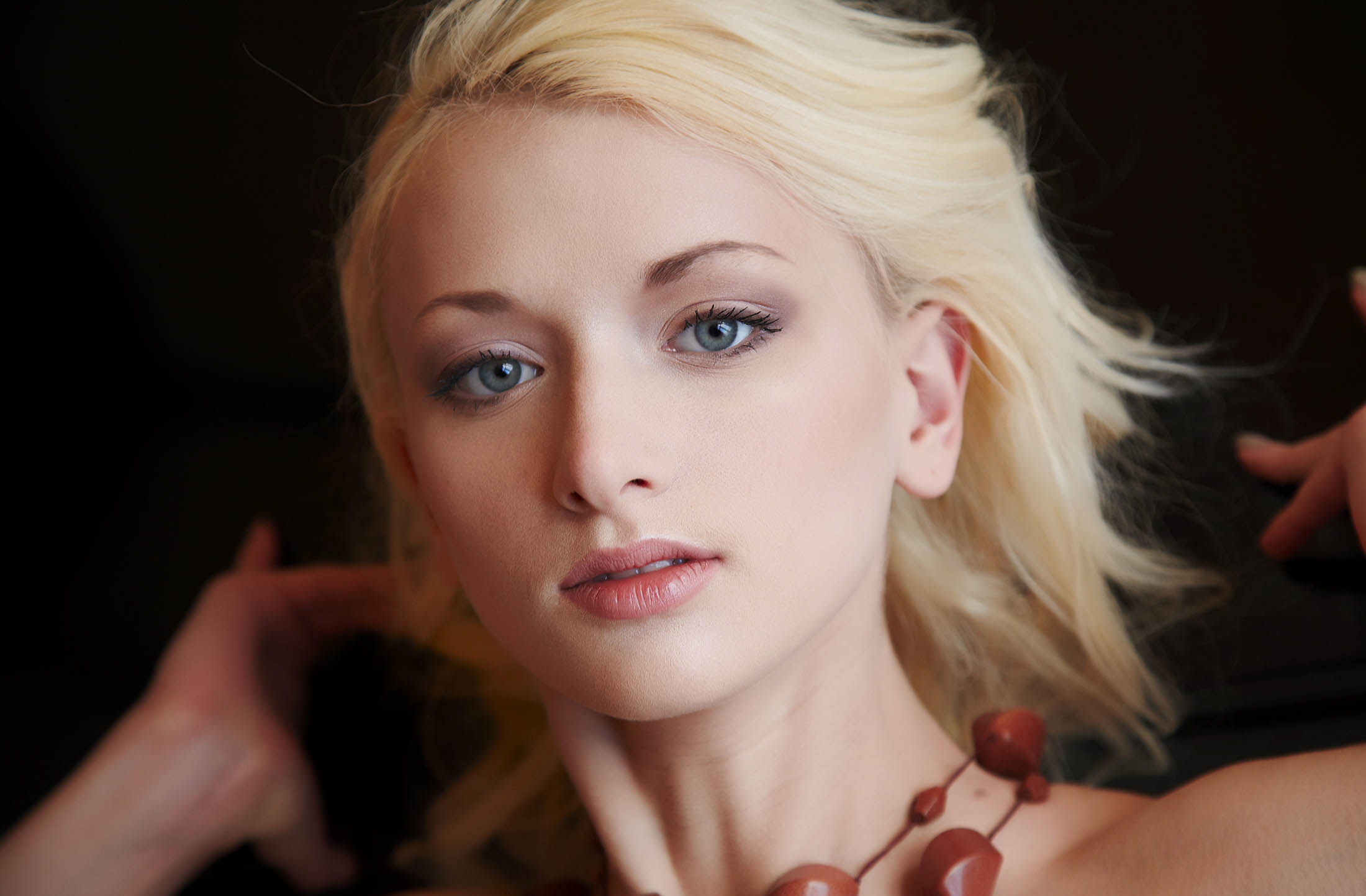 young blonde girl with blue eyes reveals her red necklace on the floor carpet in the orange bedroom