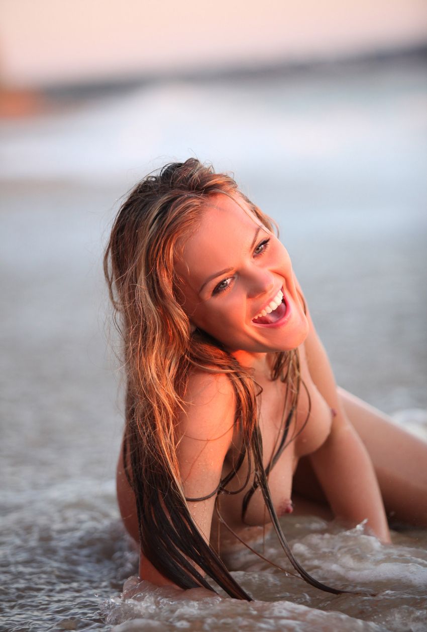 young blonde girl reveals her red blouse with white dots on the beach at the sea