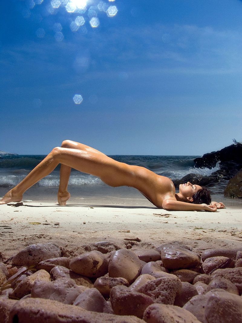 curly brunette girl reveals her body with necklaces at the sea on the rocky shore
