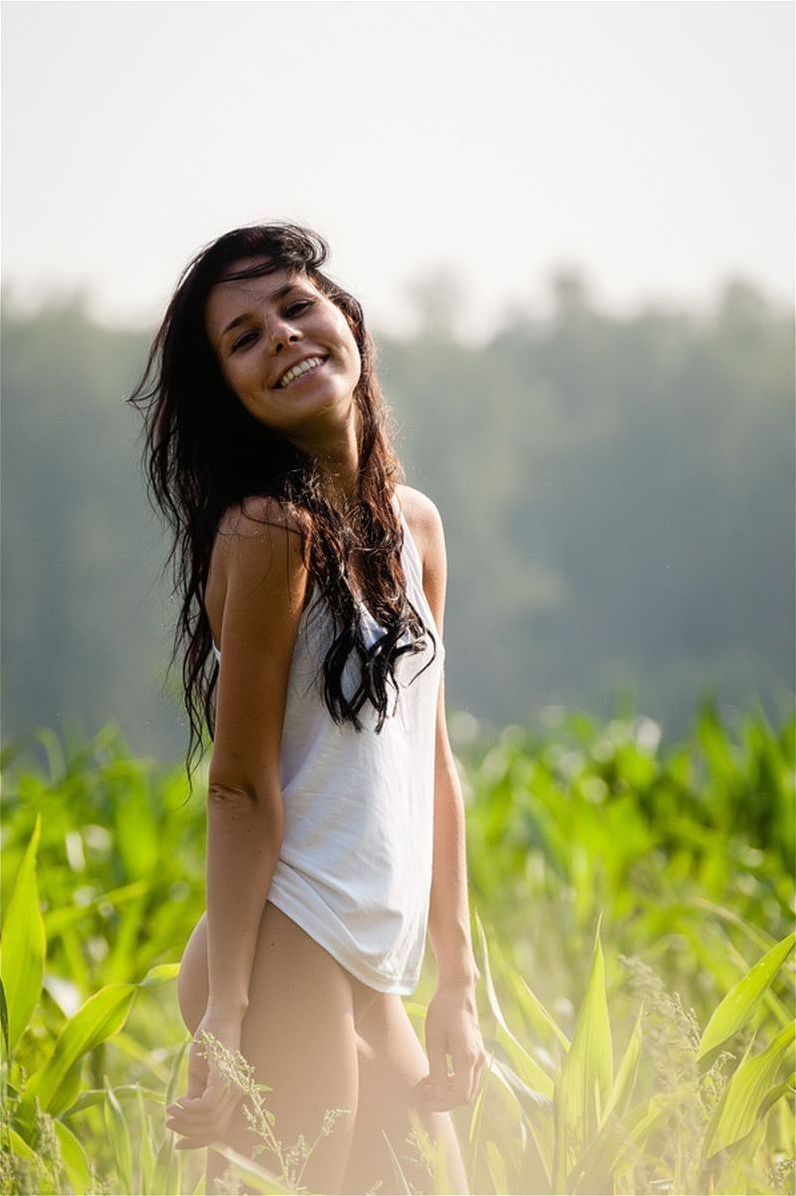 young red haired girl undresses her white sleeveless shirt on the green field outside in the nature